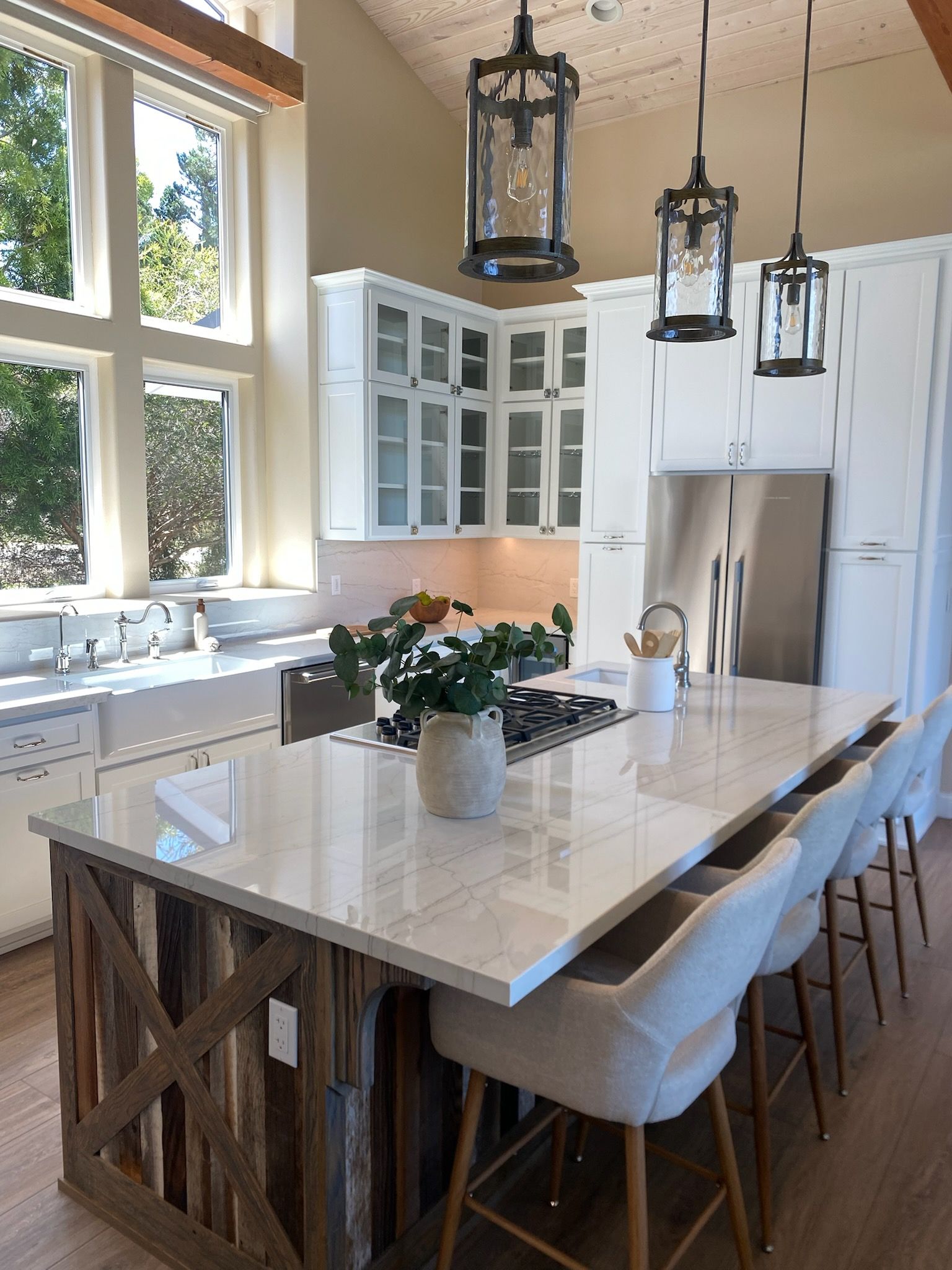 Bright modern kitchen with white cabinets, large island, pendant lights, and stools by a sunlit window.