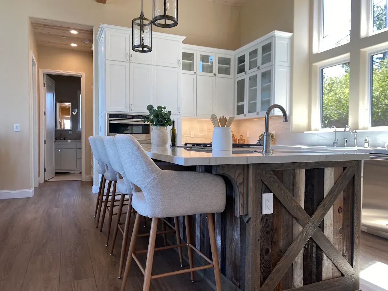 Bright kitchen with island, white cabinets, bar stools, and large windows overlooking trees