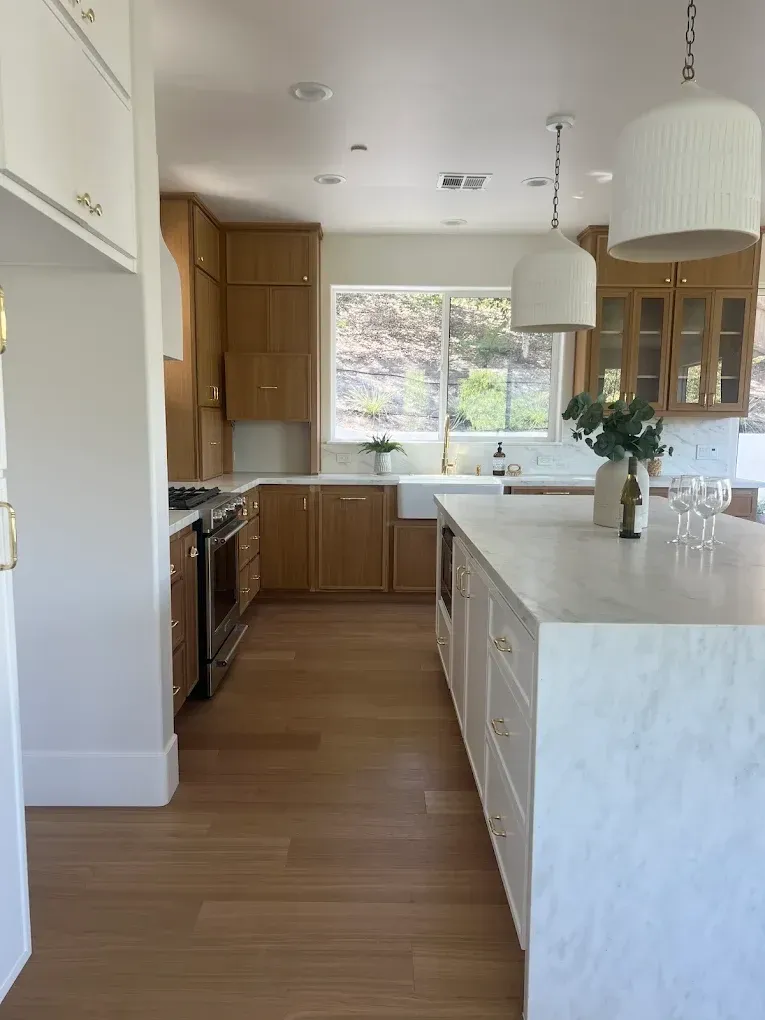 Bright modern kitchen with wood cabinets, white island, and large window overlooking trees.