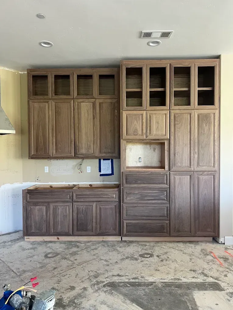 Built-in wooden cabinets and drawers in a kitchen, with unfinished floors and a small countertop area.