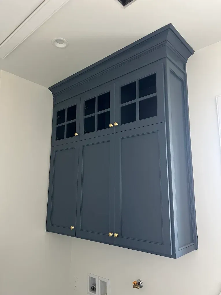 Dark blue wall-mounted cabinet with glass-front upper doors in a white room