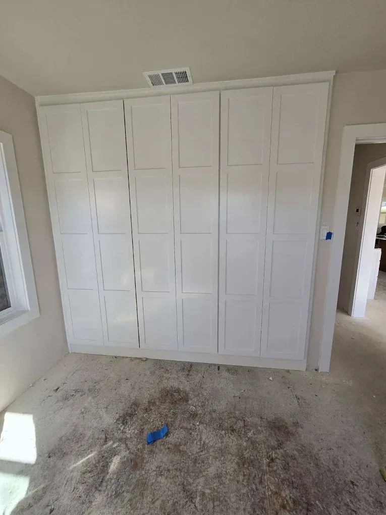 White built-in closet doors in a dusty, unfinished room with bare carpet and light walls