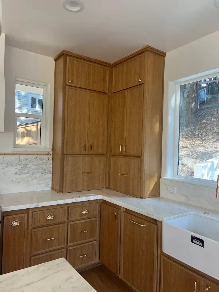 Corner kitchen with wood cabinets, white countertops, and two windows on either side.