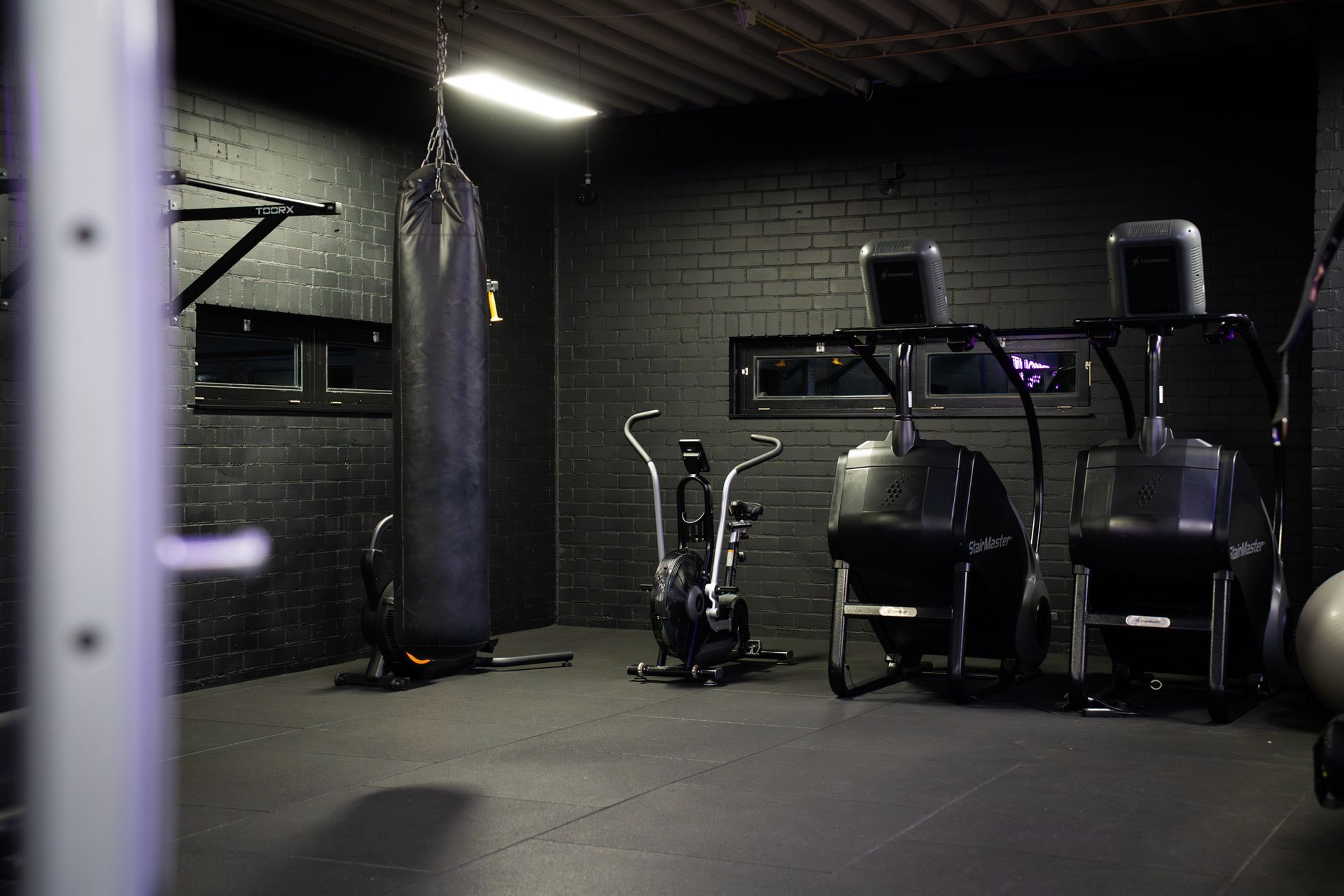 Een schemerige sportschool met een zware boksbal, een hometrainer en fitnessapparaten in een donkere ruimte.
