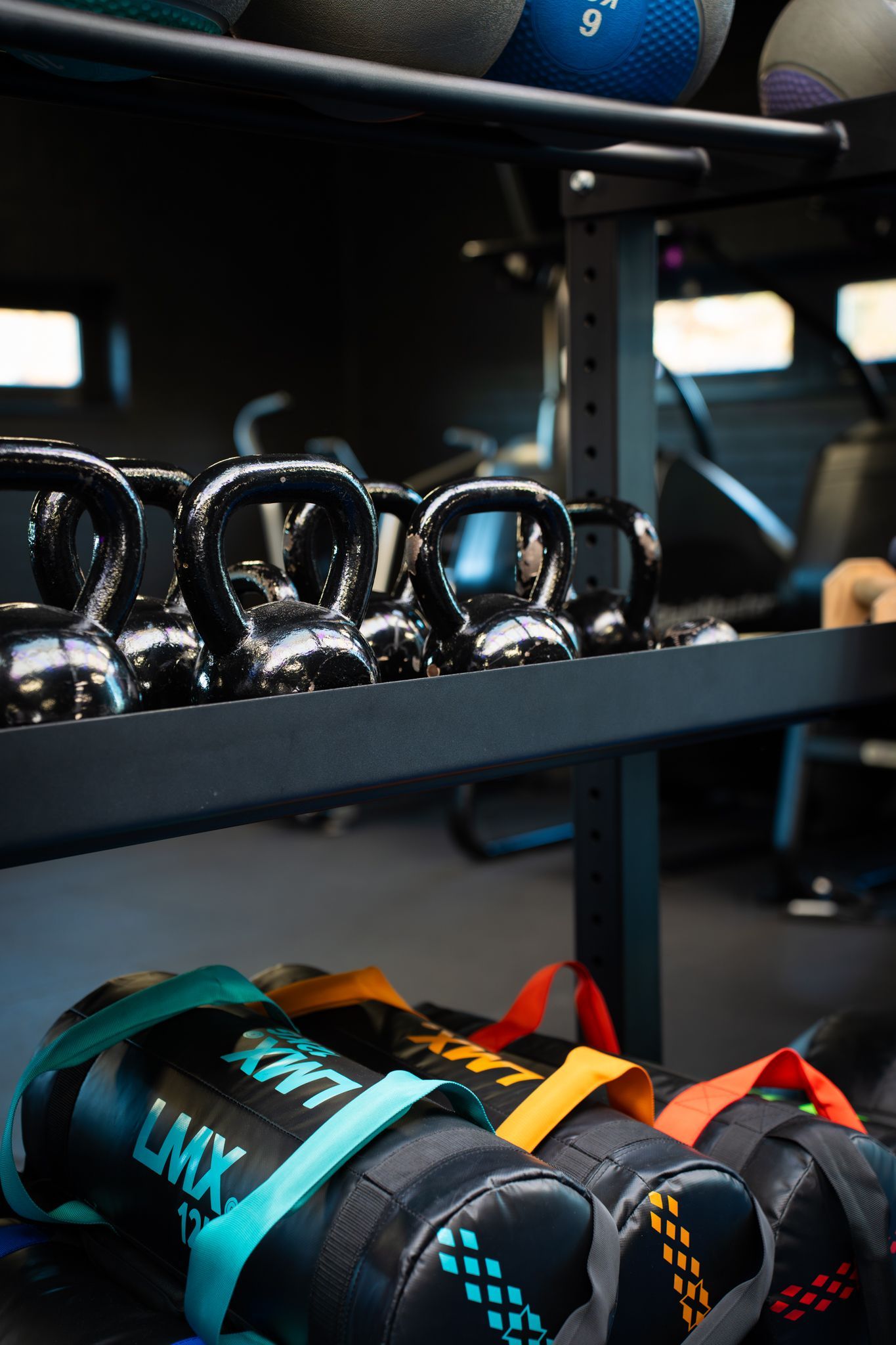 Schappen met zwarte kettlebells en kleurrijke verzwaarde zandzakken in een opslagruimte van een sportschool.