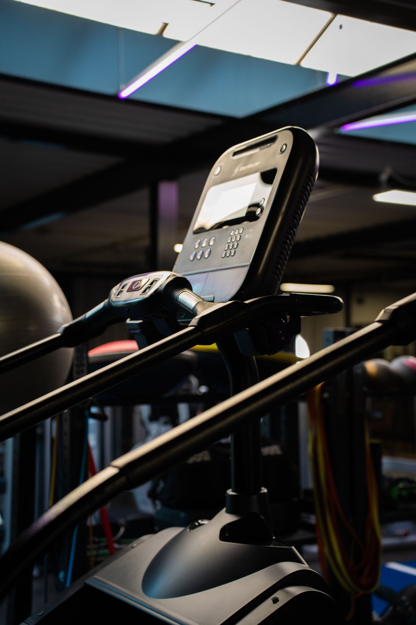 Telefoon gemonteerd op een loopband in een schemerige sportschool met neonverlichting aan het plafond.