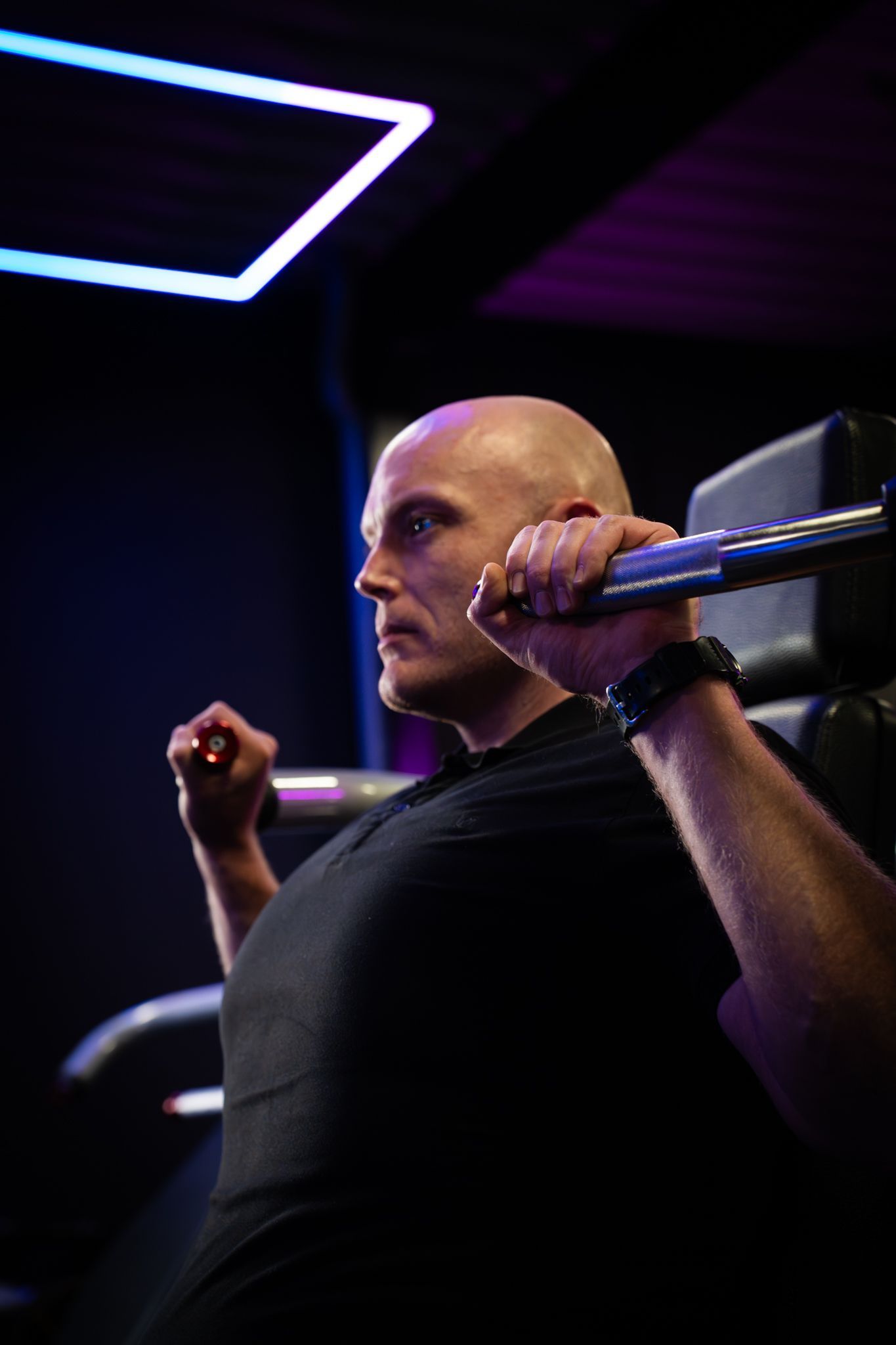 Een persoon tilt een halter op in een donkere sportschool met paarse verlichting.