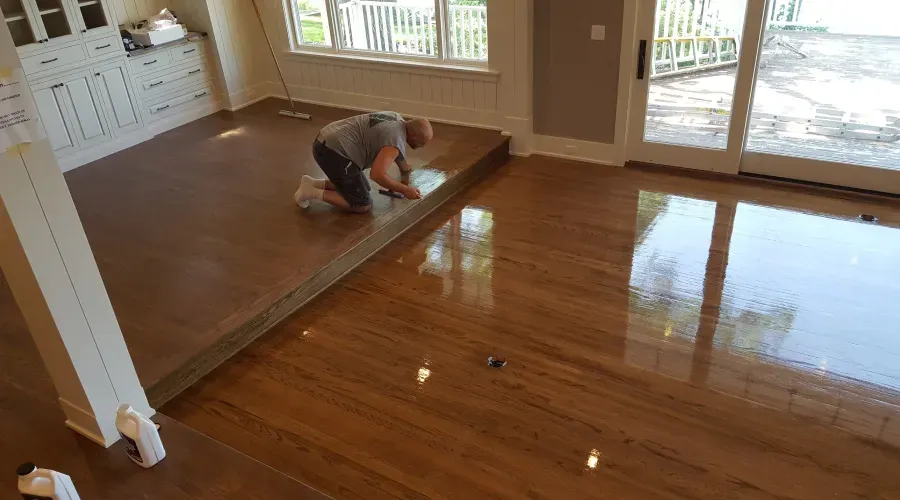 A man is kneeling on a wooden floor in a living room.