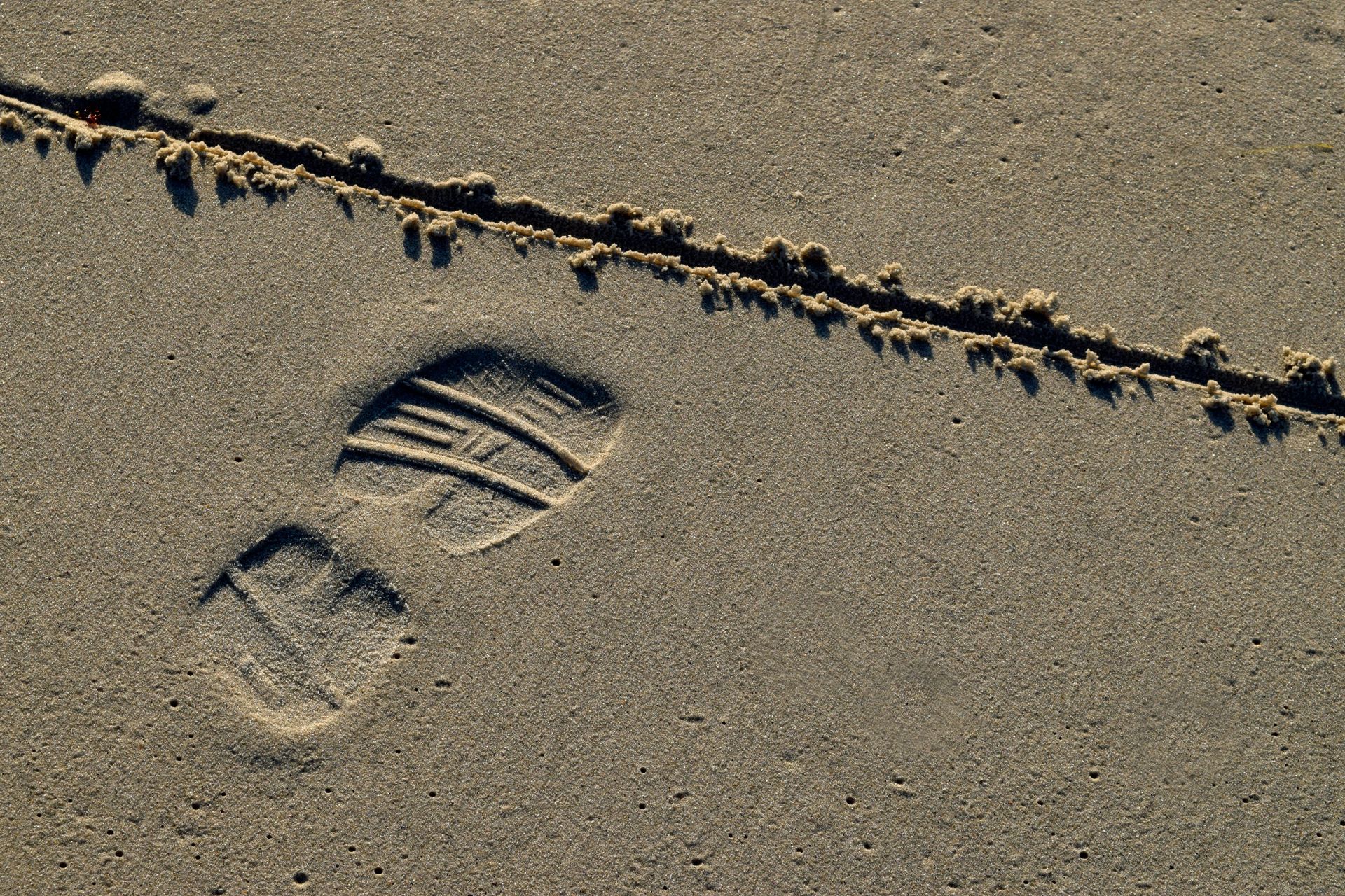 A close-up of a footprint in the sand on a beach with a line drawn in front of it