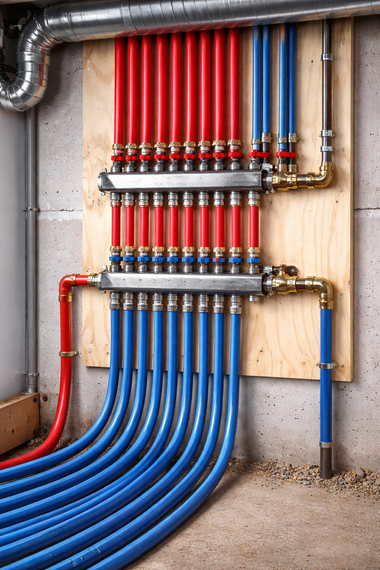 Red and blue PEX tubing connected to a manifold on a wooden board against a concrete wall.