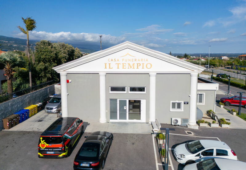 Vista frontale dell'edificio del Tempio con auto parcheggiate davanti, sotto un cielo sereno.