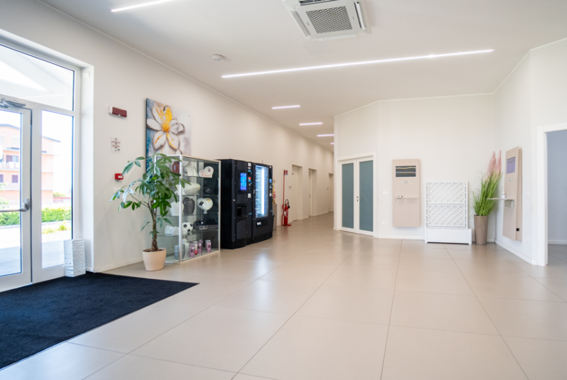 Luminosa hall moderna con pavimento piastrellato, distributori automatici, porta a vetri e una pianta in vaso.
