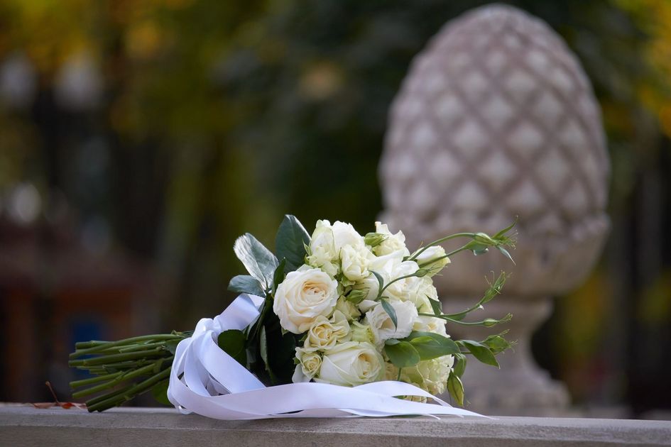 Bouquet di fiori bianchi con nastro su una sporgenza di pietra, all'aperto, con sullo sfondo un monumento sfocato a forma di ananas.