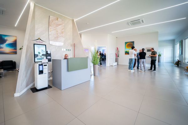 Luminosa hall moderna con un chiosco, un banco reception e diverse persone in piedi vicino alla parete di fondo.