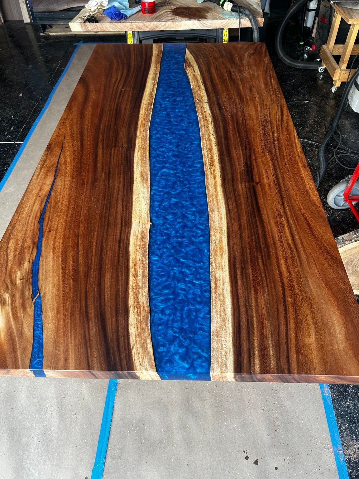 Wood slab with a bright blue resin center, set on a workbench in a workshop.