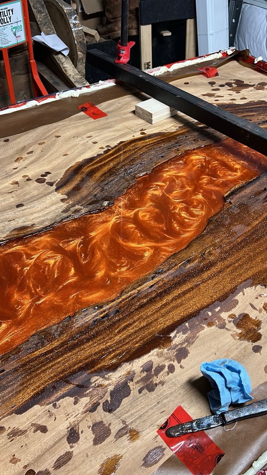 Close-up of orange resin poured into a wood slab, clamped on a workbench during a woodworking project.