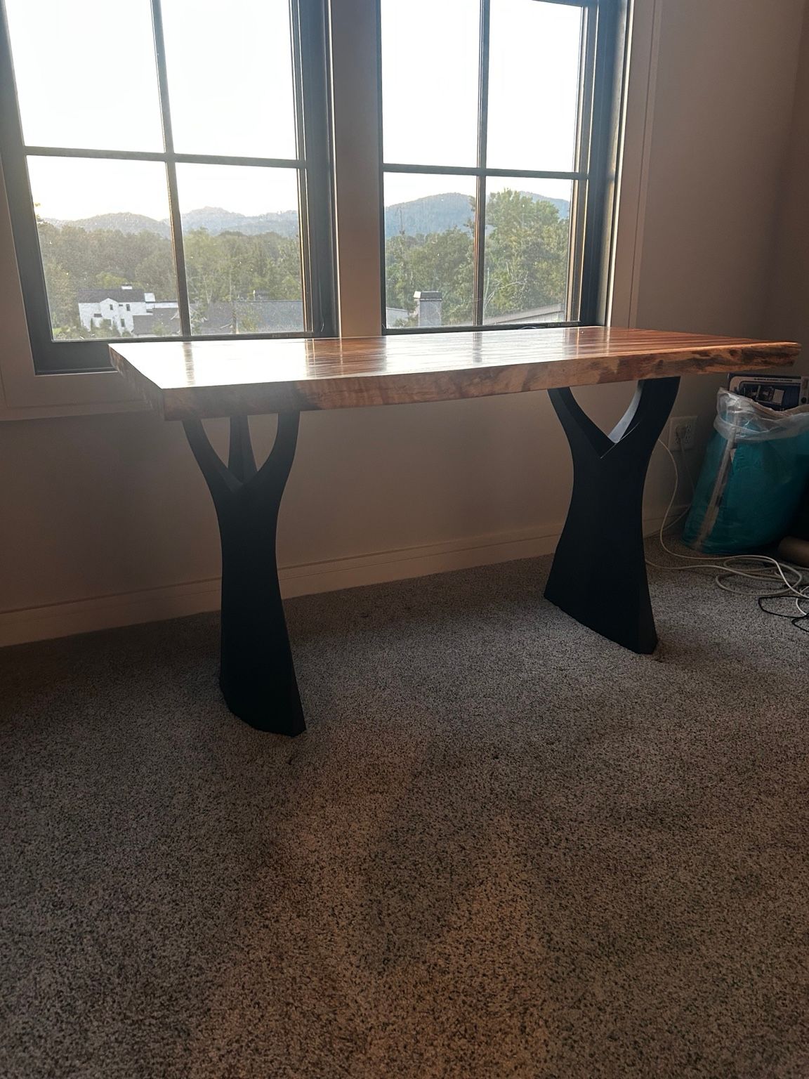 Wooden table with black metal legs by a window, overlooking a mountain view.