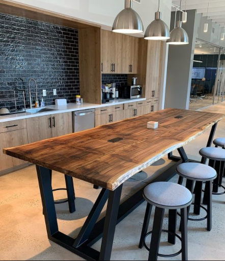 Office break room with a long wooden table, stools, and kitchen cabinets.