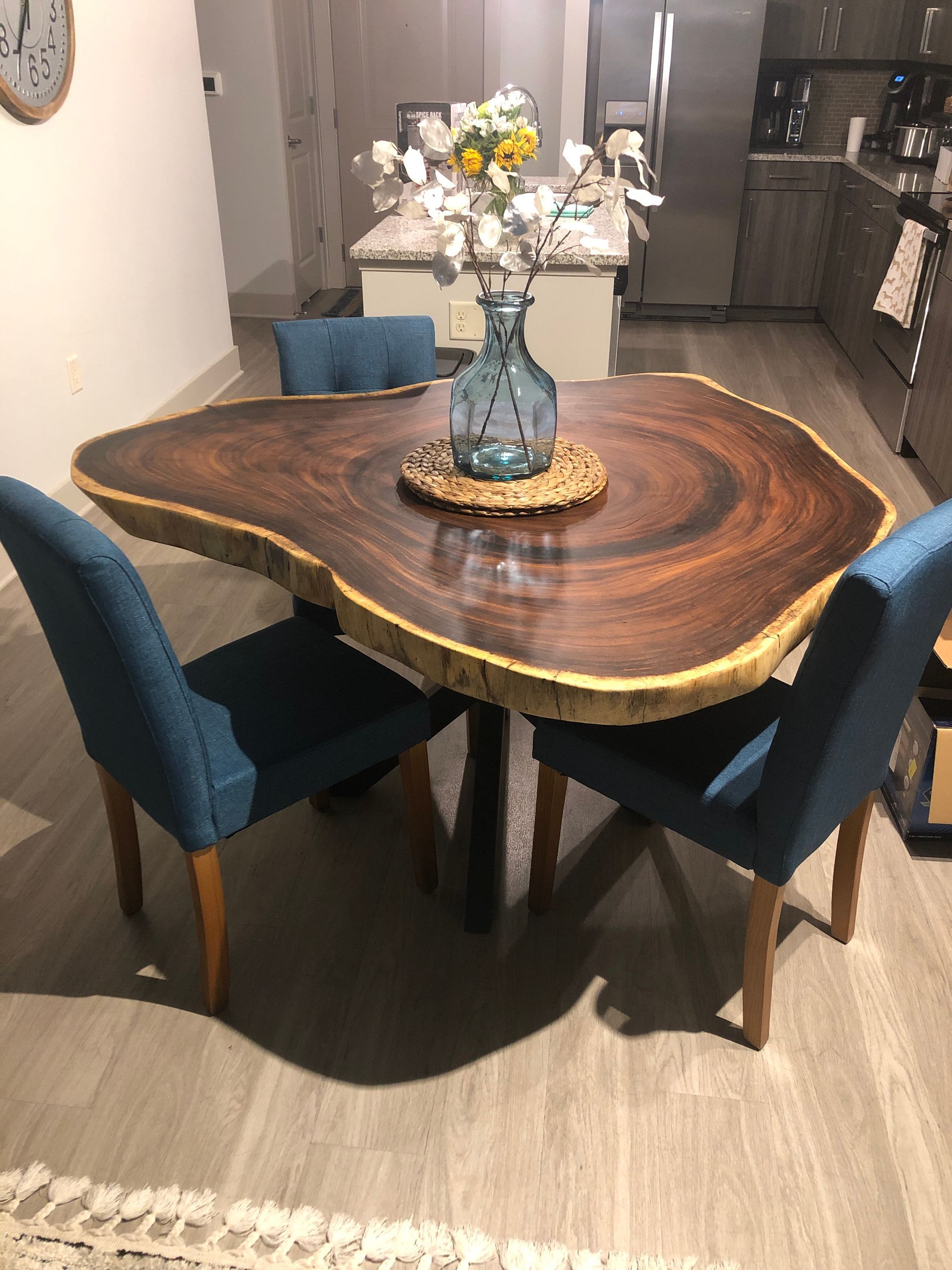 Live edge wooden dining table with blue chairs and vase of flowers.