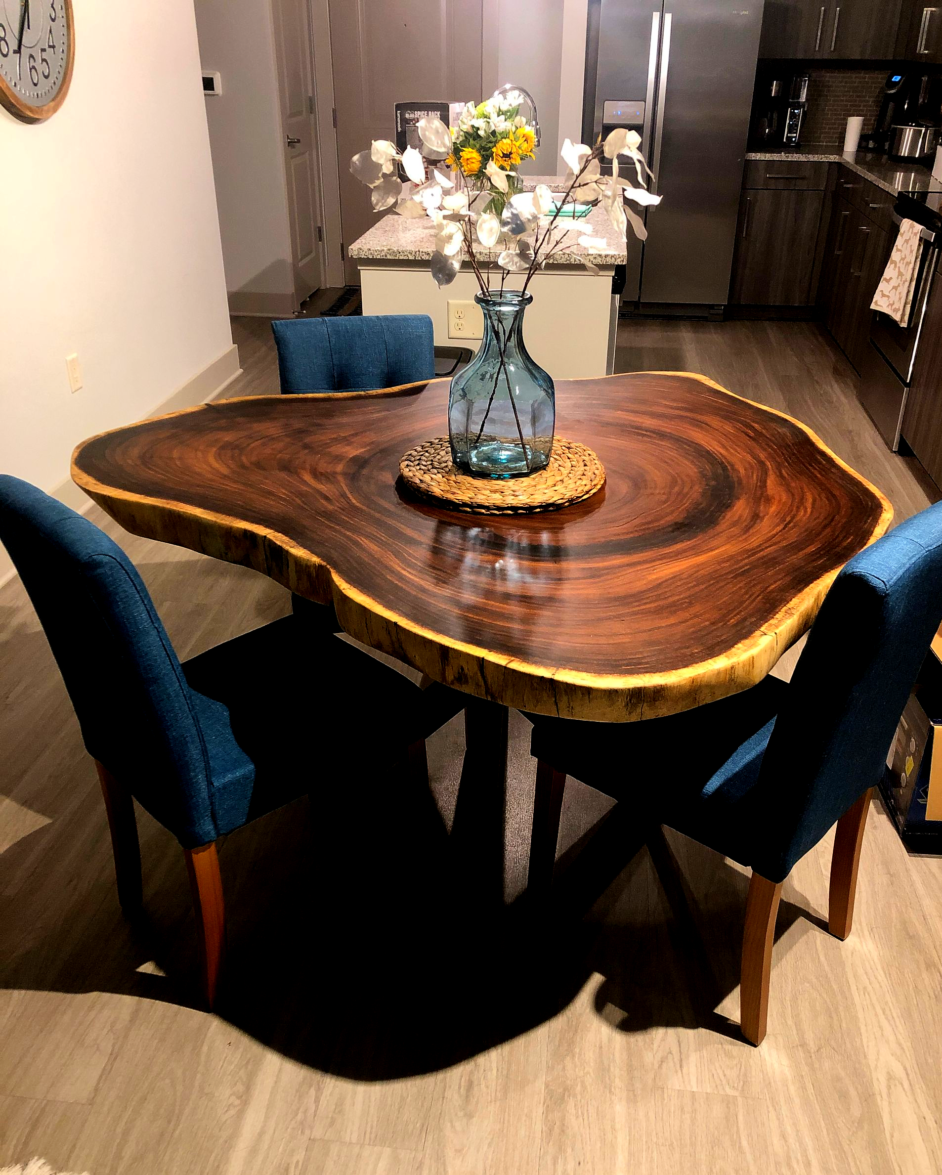 Round wooden dining table with blue chairs and a flower vase in a kitchen-dining area