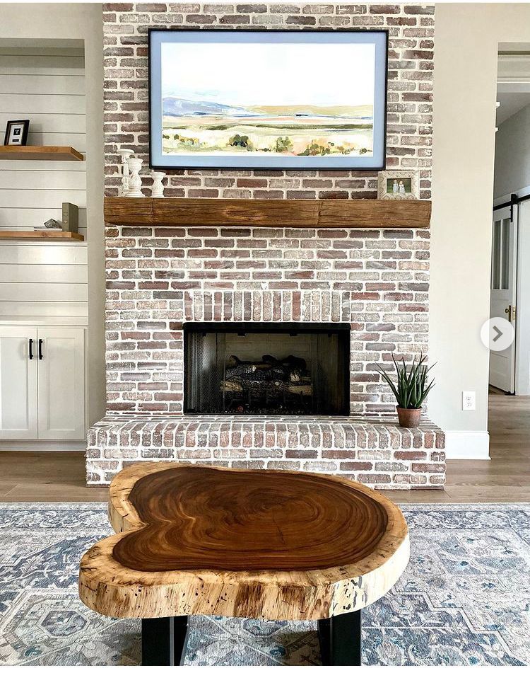 Living room with a brick fireplace, wooden mantle, TV, and live-edge coffee table on a rug.