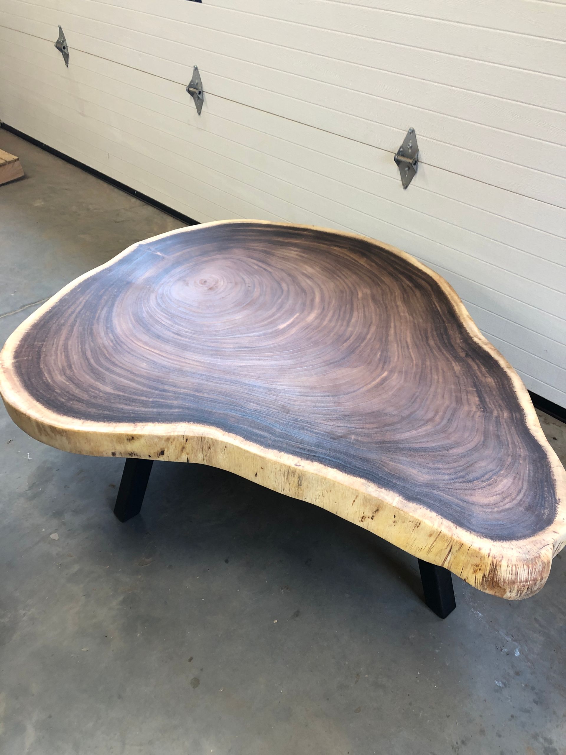 Live-edge wood coffee table with dark wood grain, resting on black metal legs, indoors.
