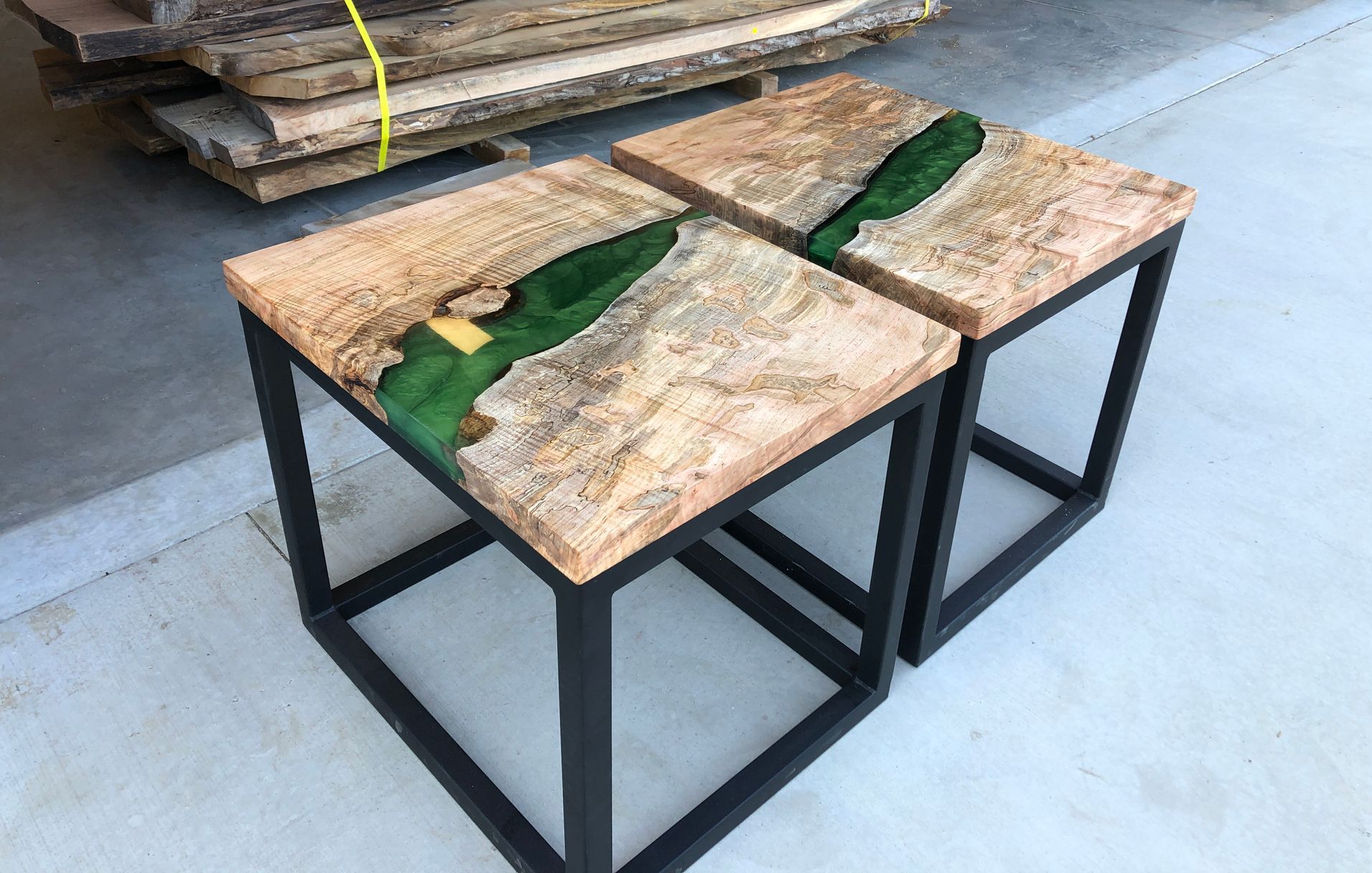 Two square wooden side tables with live edge tops and green epoxy resin insets, on black metal frames, outdoors.
