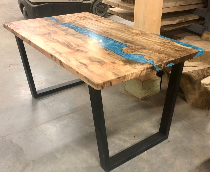 Wooden table with a blue resin river top and black metal legs in a workshop.