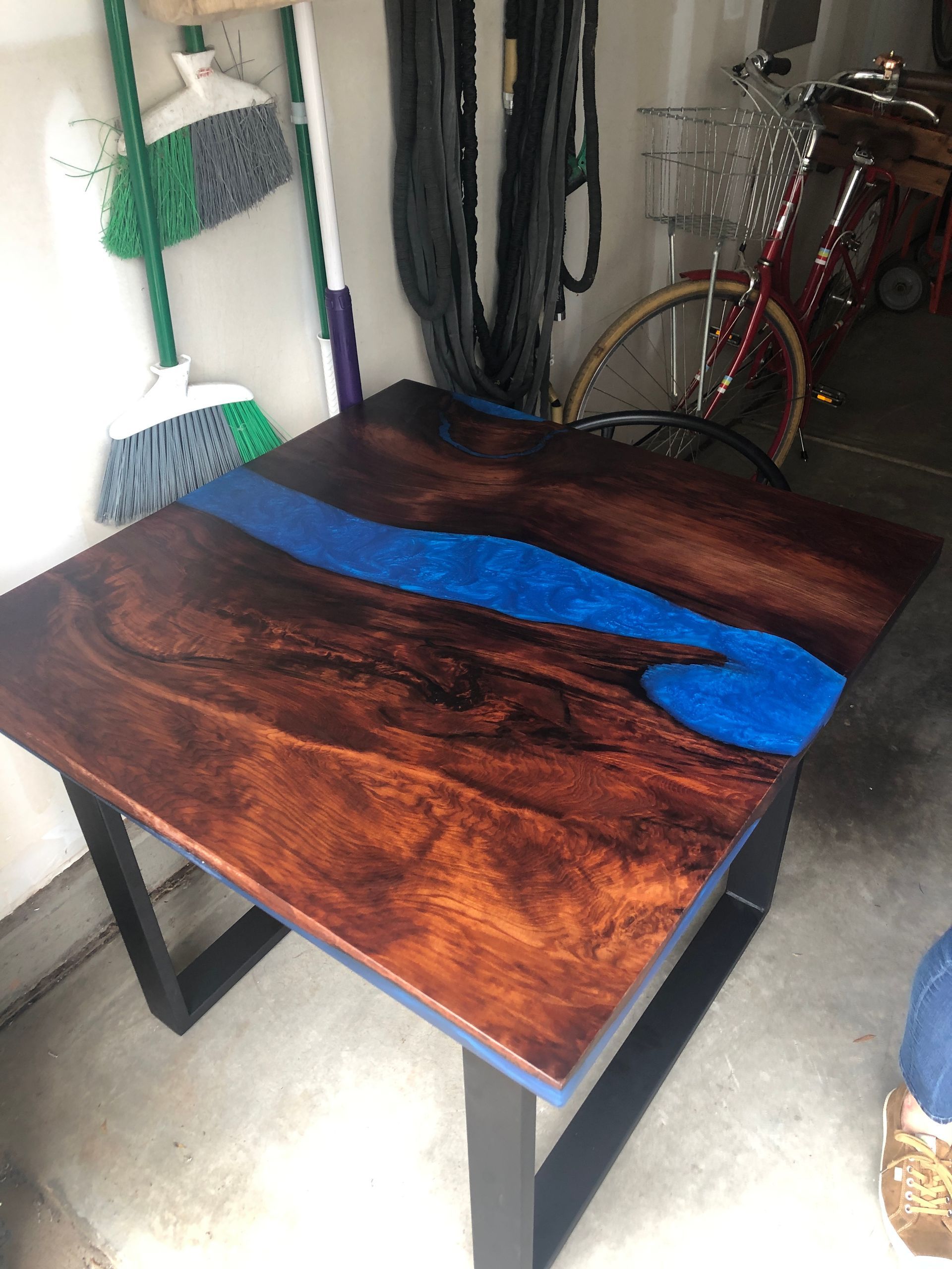 Wooden table with blue epoxy river and black metal legs. Garage setting.