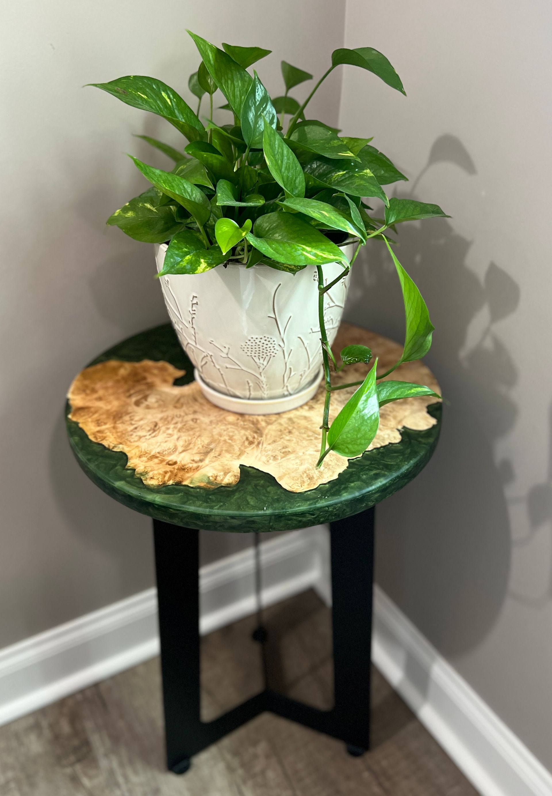 Green pothos plant on a unique side table with a green border and wooden tabletop, black legs.