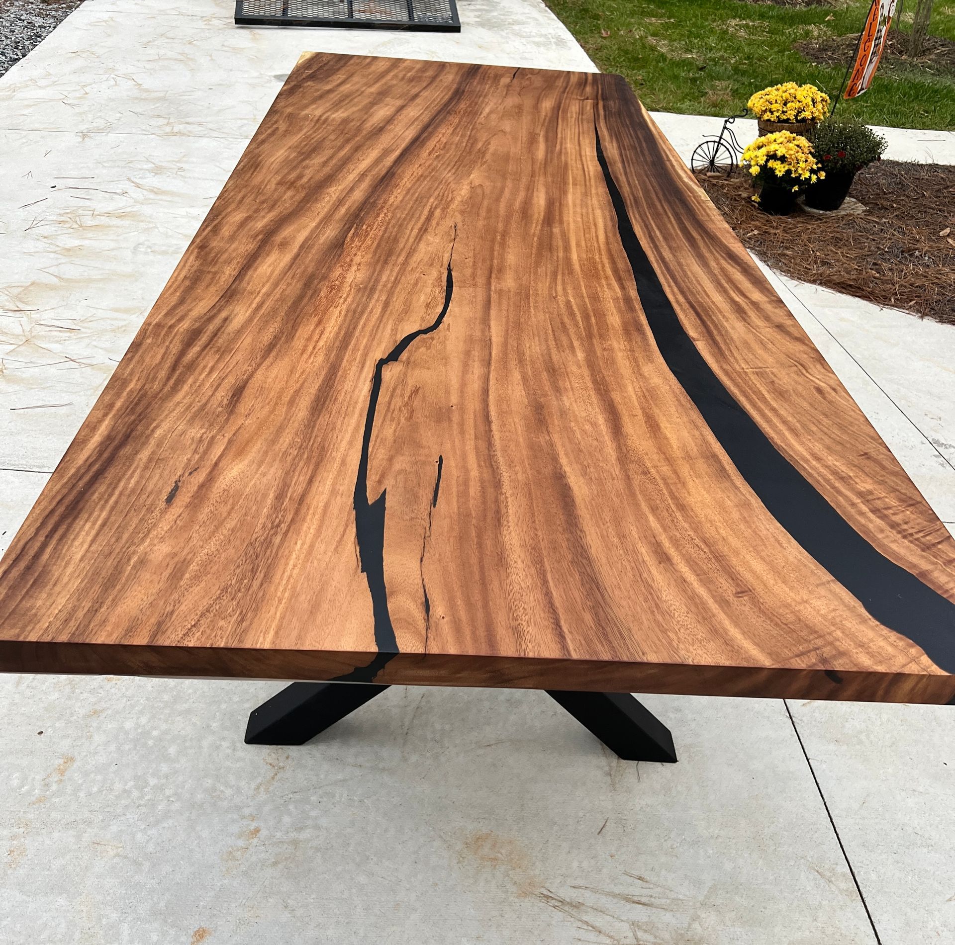 Wooden table with black epoxy river and metal base, outdoors.