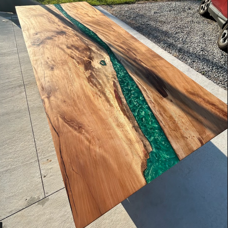 Wood slab tabletop with a green resin river inset, shown outdoors on pavement.