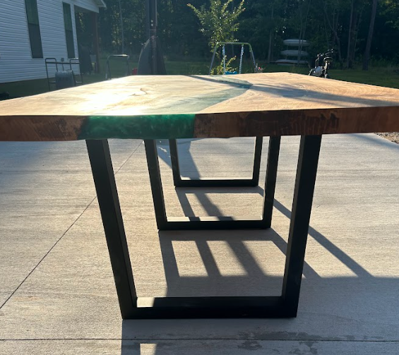 Wooden table with green epoxy river, black metal legs, outside.