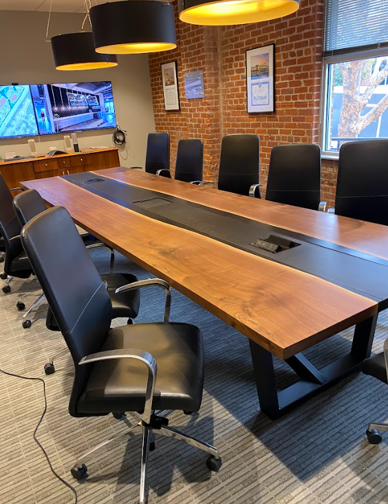 Conference room with long wood table, black chairs, brick wall, and overhead lights.