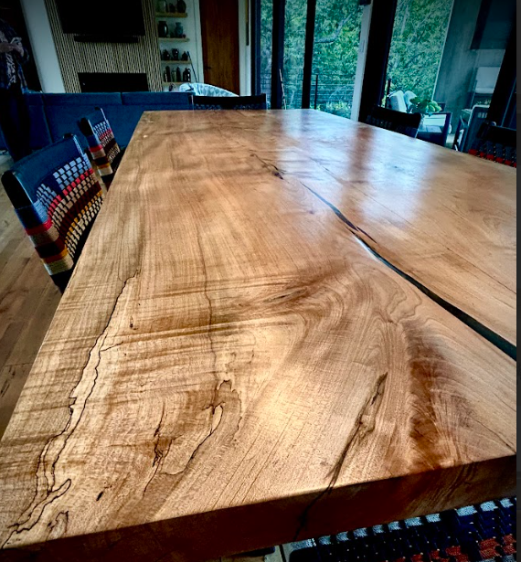 Wooden dining table with visible wood grain and a dark crack. Chairs with patterned backs.