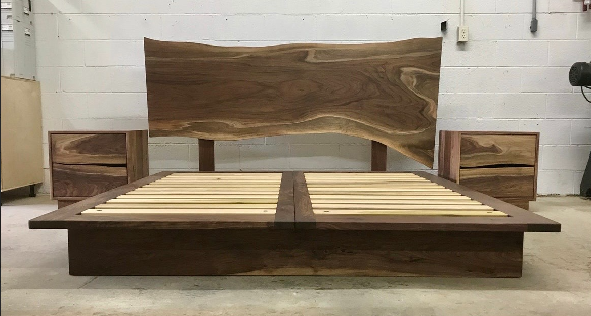 Wooden bed frame with slatted base and tall live-edge headboard in a workshop showroom