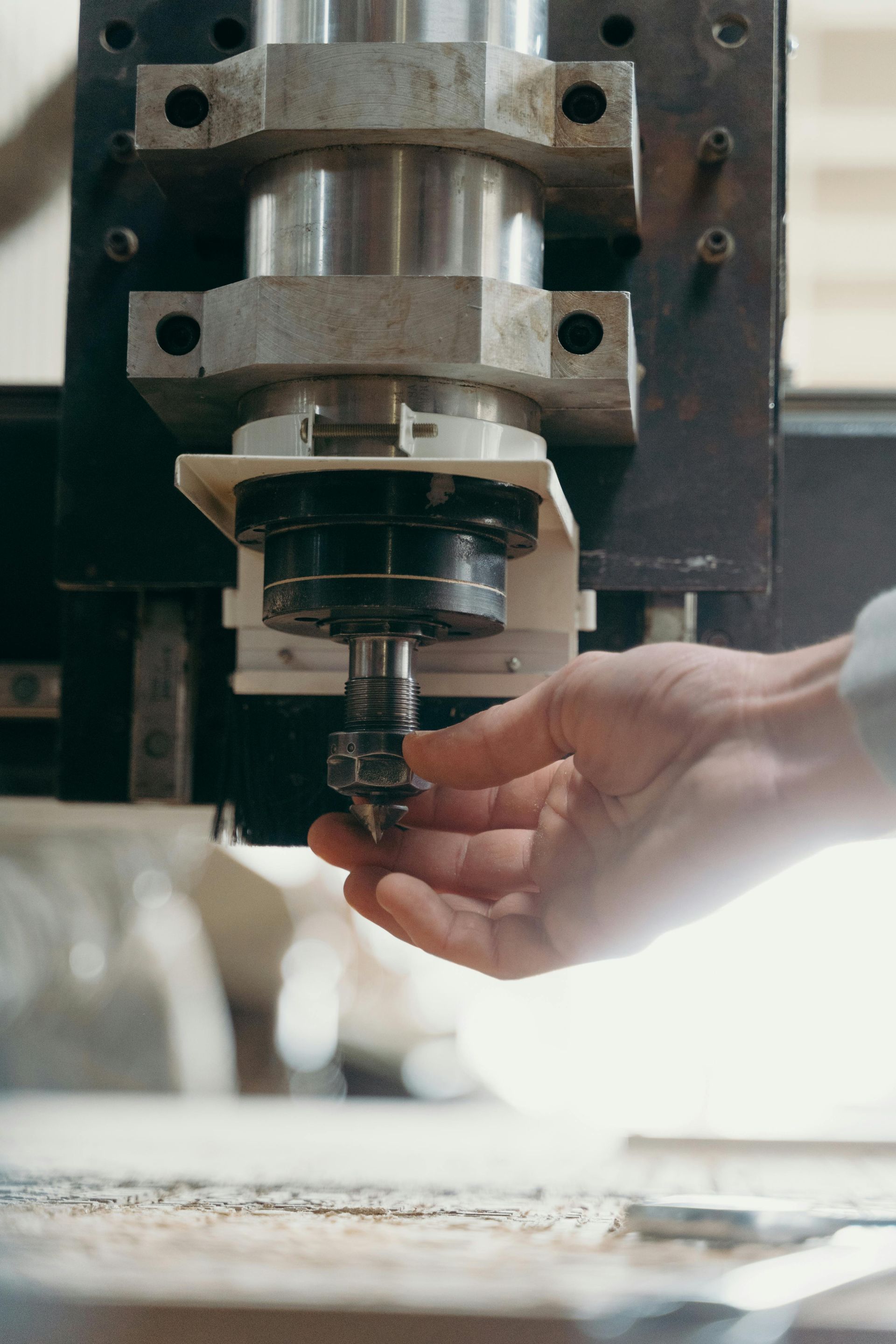 Hand guiding a drill press bit over a work surface in a workshop