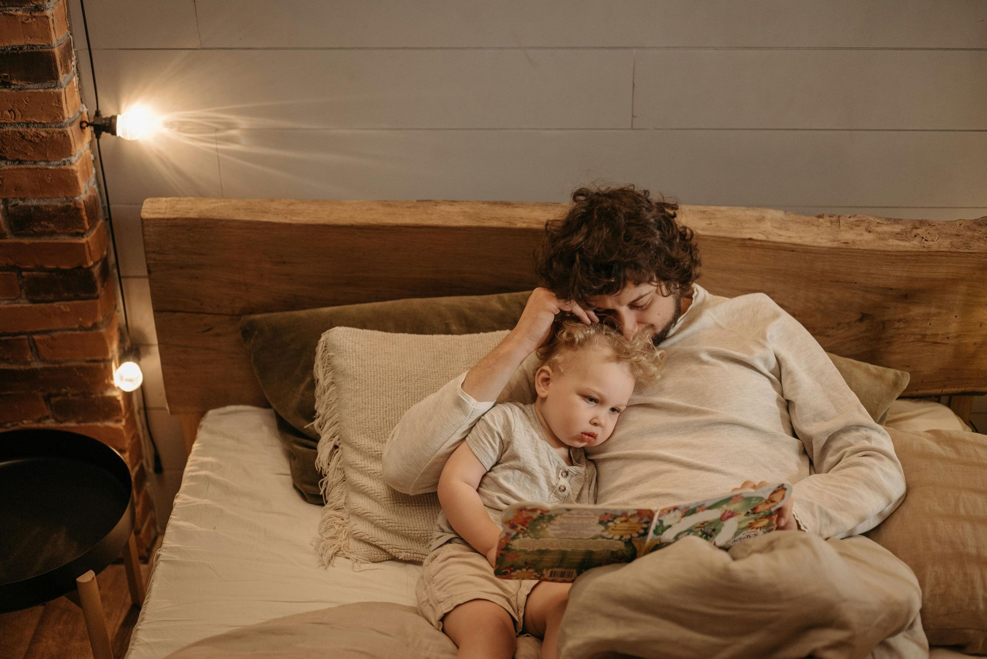Man reading a book to a child in bed; warm lighting and cozy setting.