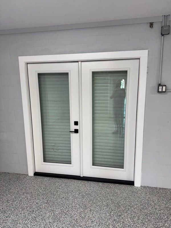 White double glass doors with blinds in a gray exterior wall.