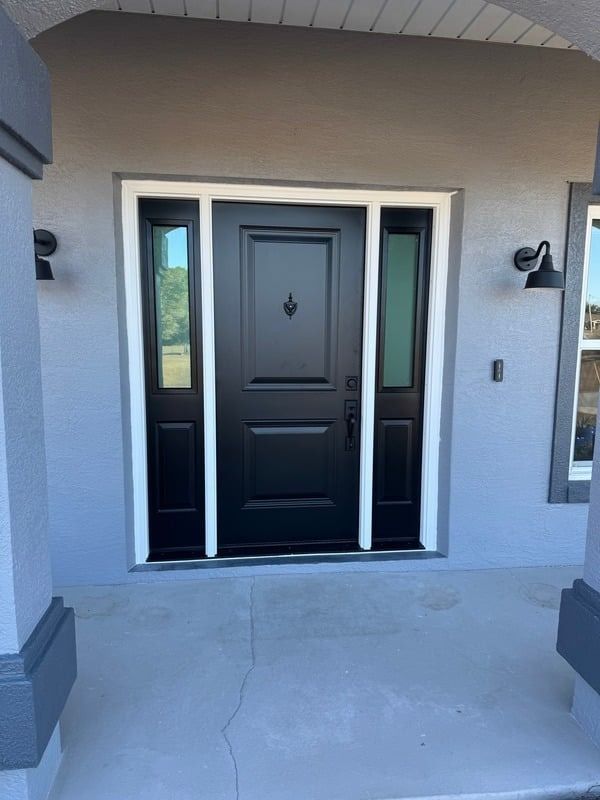 Front entry with black door, sidelights, and gray stucco exterior under a covered porch