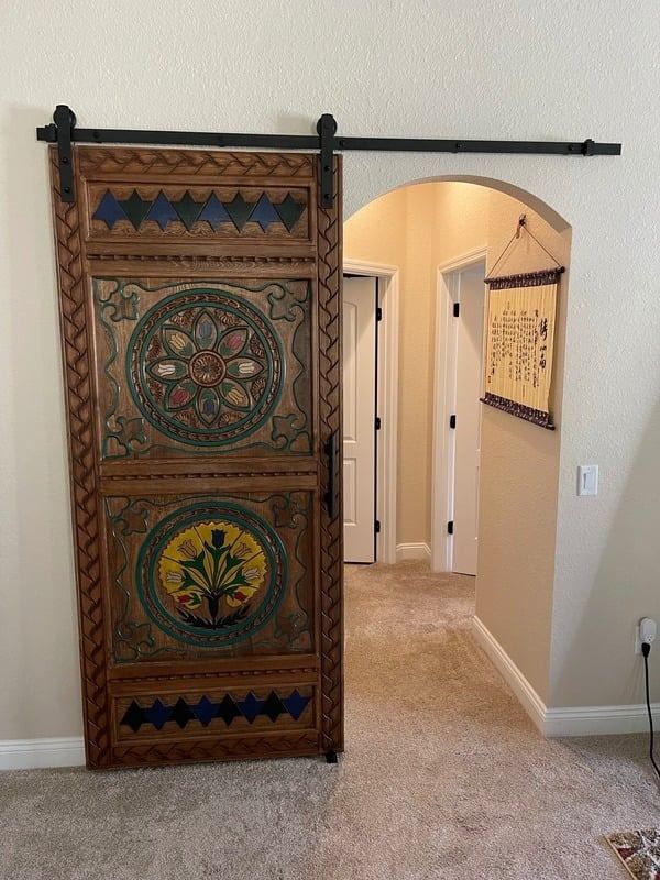 Decorative wooden sliding barn door with colorful circular designs in a carpeted hallway doorway