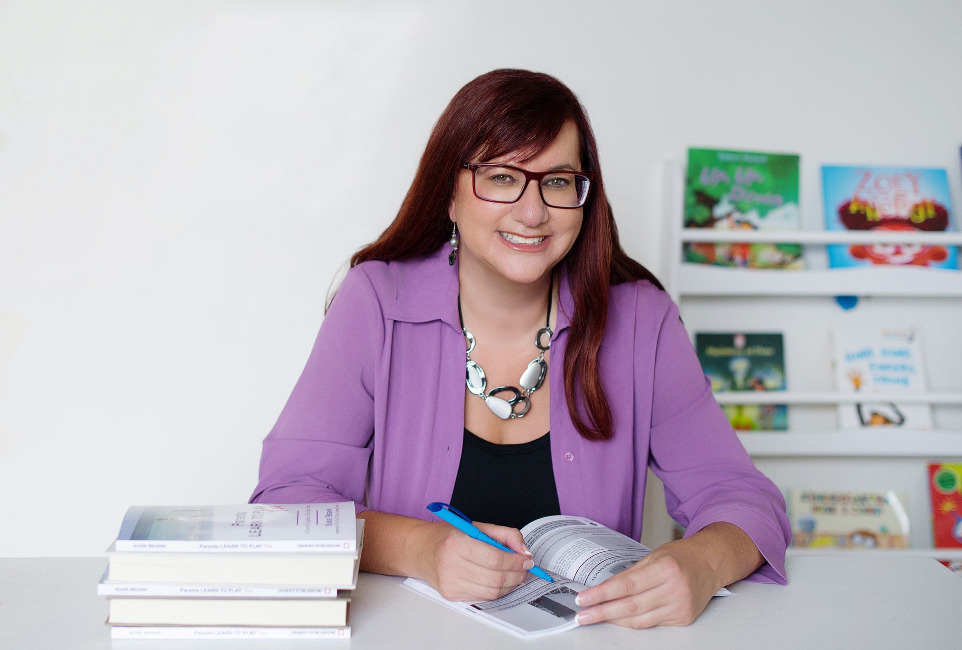Susie Beghin smiling at her desk with her books.