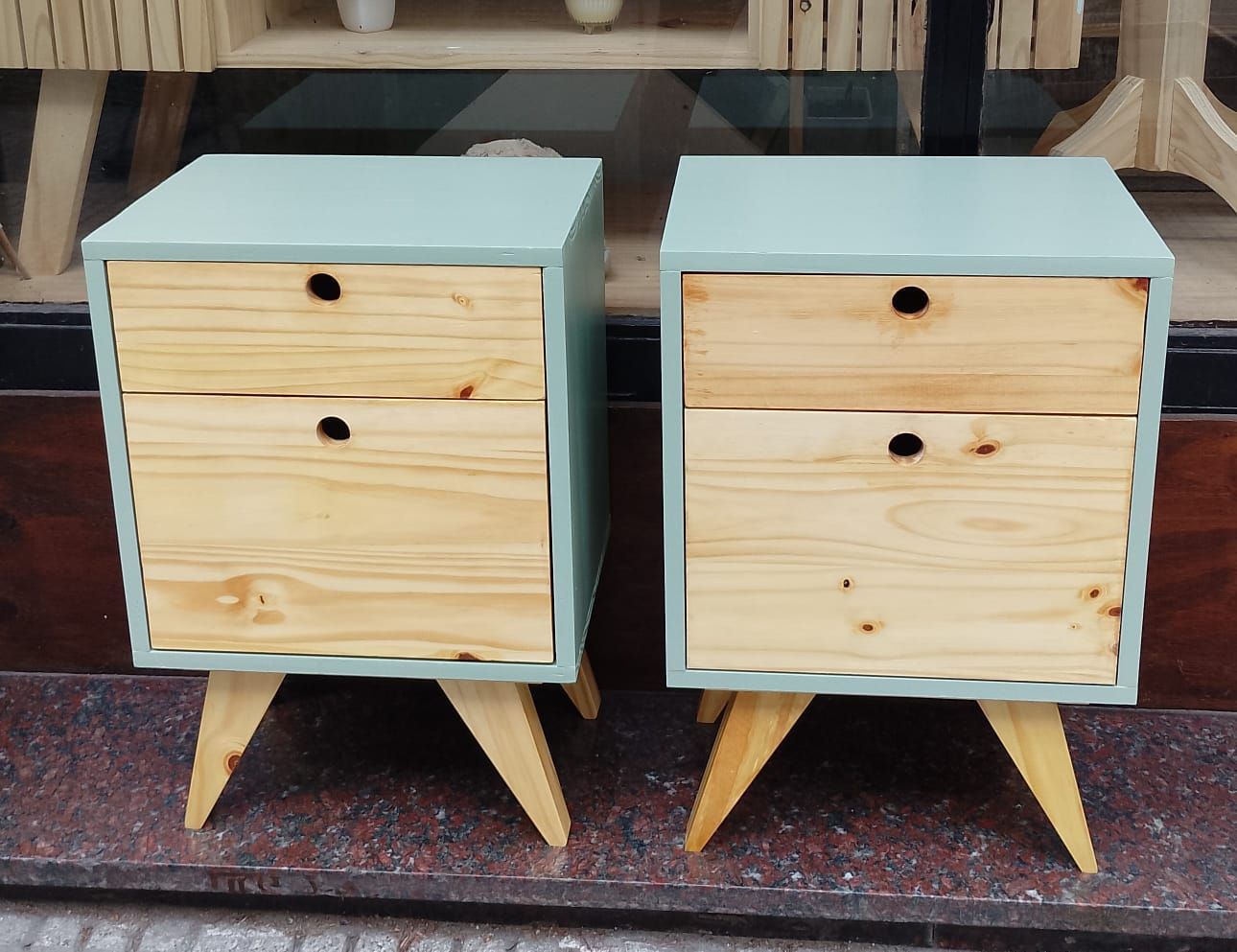 Dos mesitas de noche de color azul claro con dos cajones de madera cada una, colocadas sobre patas de madera en ángulo.