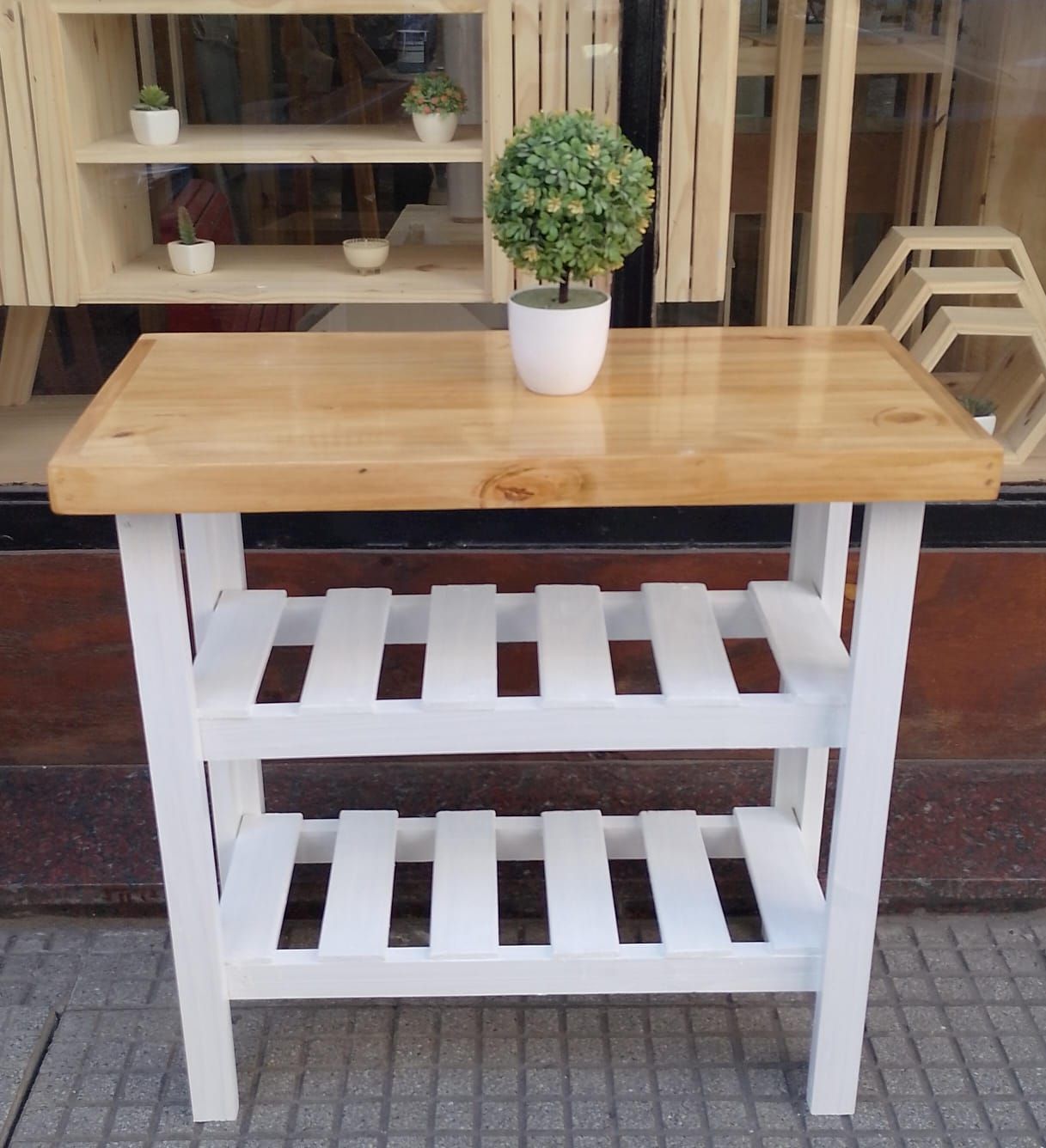 Isla de cocina de madera con encimera de color claro, estructura blanca y dos estantes de listones. Una planta sobre la encimera.