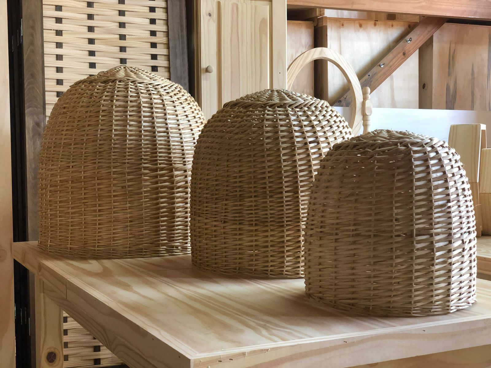 Tres pantallas de lámparas de mimbre tejido de distintos tamaños reposan sobre una superficie de madera.