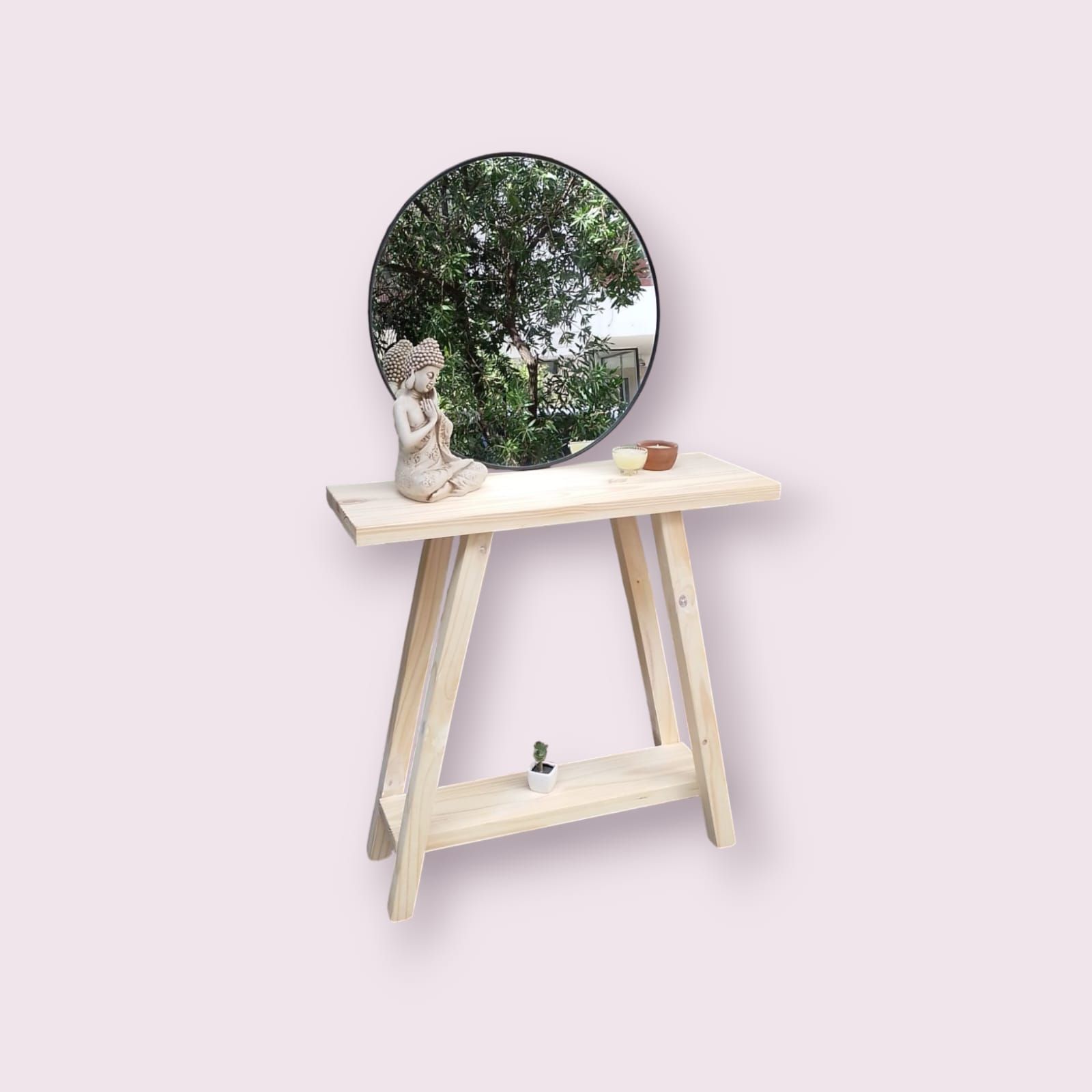 Consola de madera clara con espejo redondo, pequeño estante y decoración sobre un fondo rosa suave.