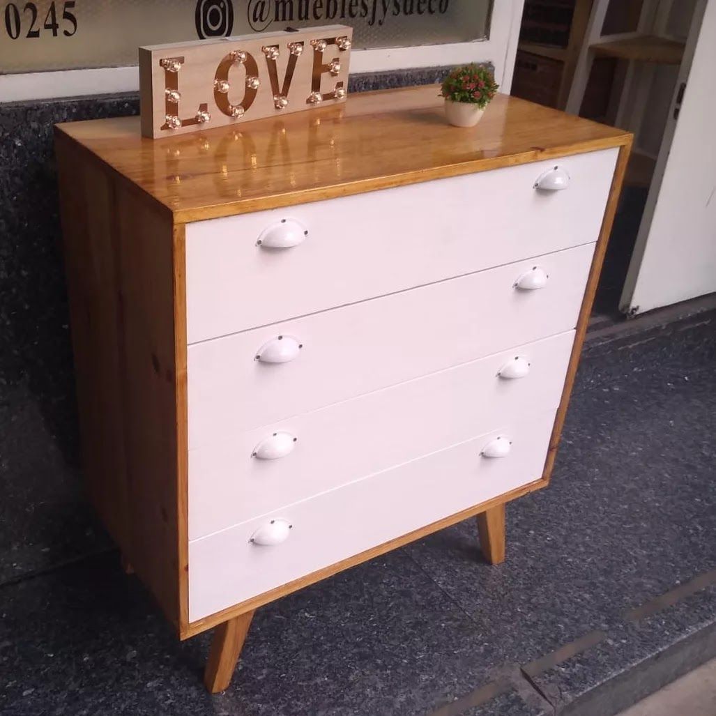 Cómoda de madera con cuatro cajones. Cajones blancos, laterales de madera clara y un letrero de 