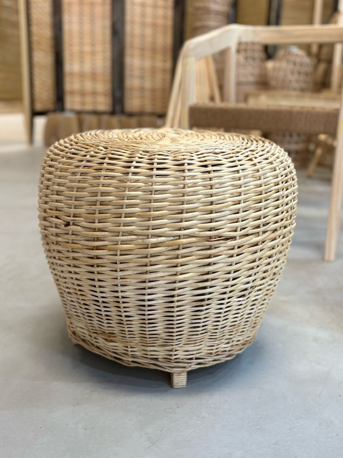 Otomana de mimbre sobre suelo claro. Tejido beige con pequeñas patas de madera.