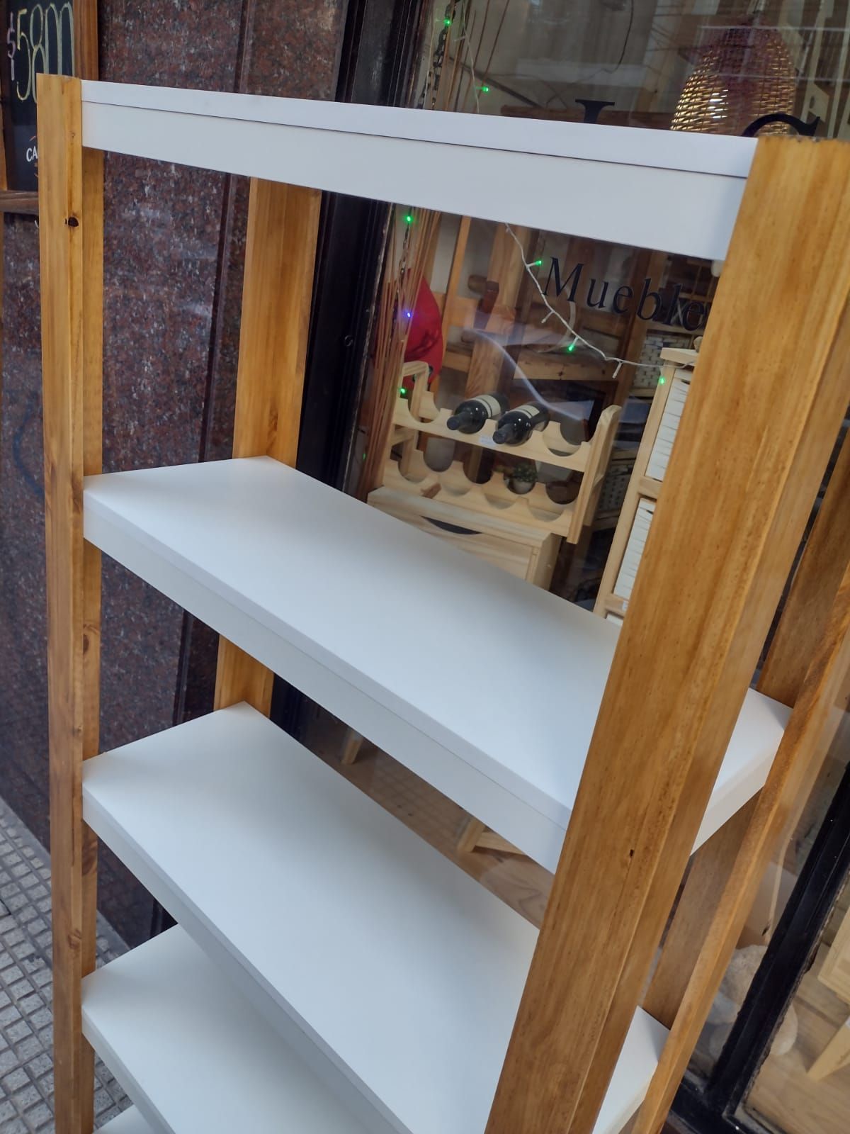 Estantería de escalera de madera con estantes blancos y marco de madera, parcialmente visible en un entorno exterior.