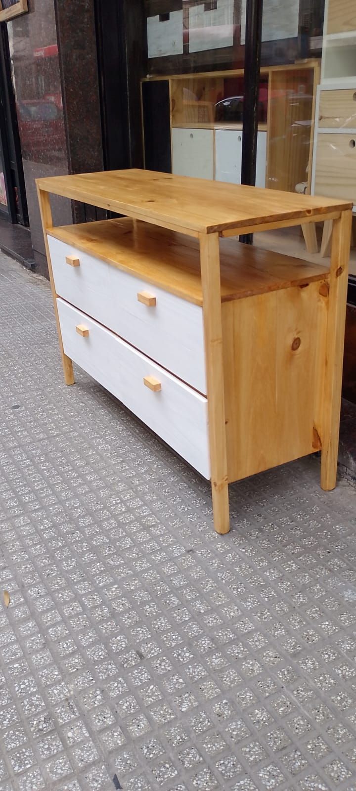 Cómoda de madera con dos cajones blancos y un estante, sobre pasarela de baldosas.